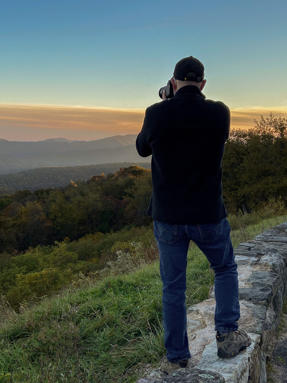 Brad Balfour perched on a wall capturing a vivid sunset